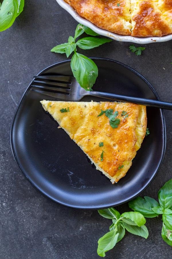 Une tranche de quiche sans pâte sur une assiette avec du basilic autour.