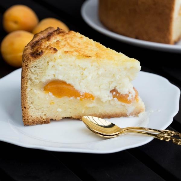 Tranche de cheesecake aux abricots sur une assiette avec une cuillère à côté.