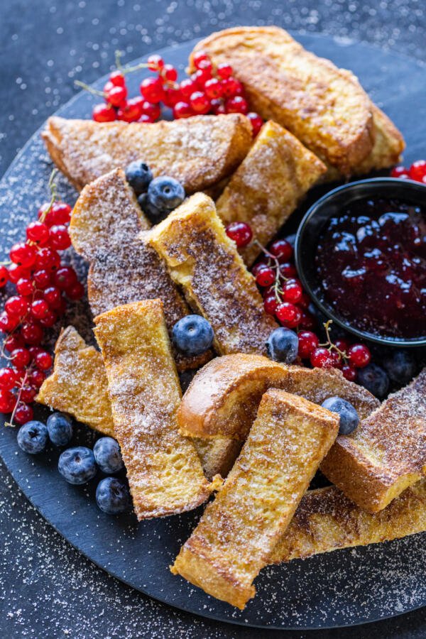 Bâtonnets de pain perdu sur un plateau de service avec des sauces et des fruits rouges.