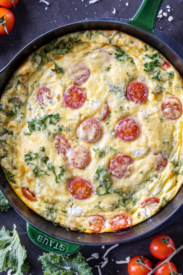 Frittata dans une poêle avec des tomates à côté.