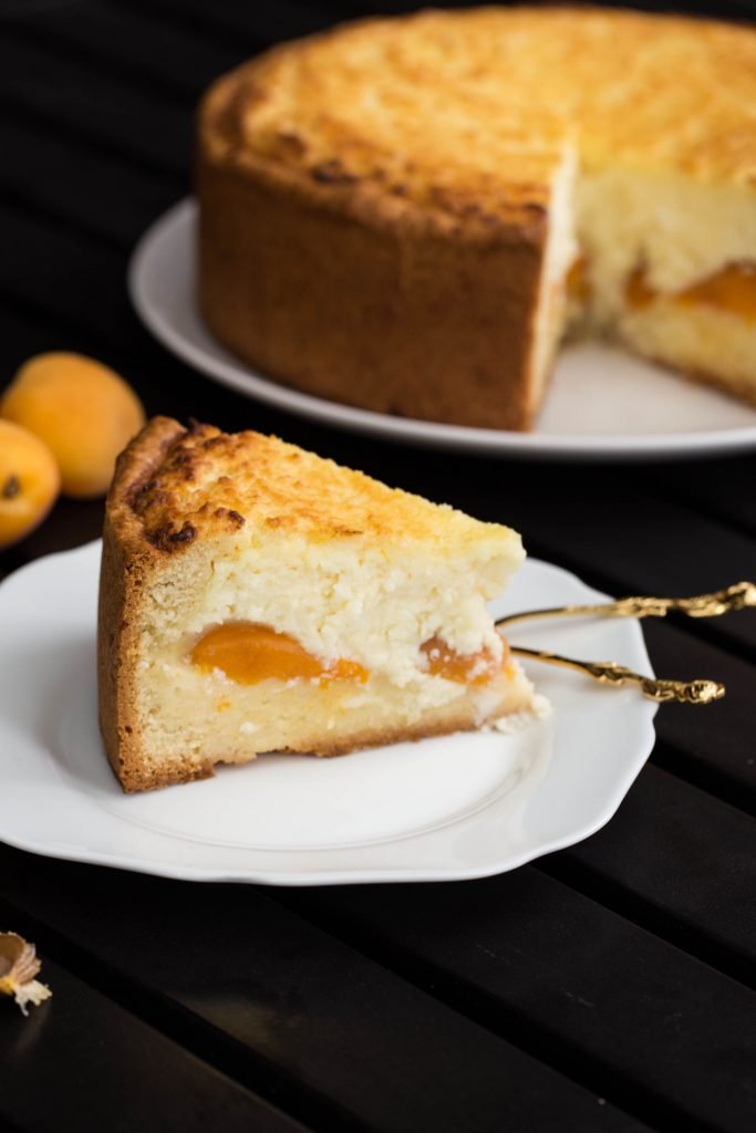Tranche de cheesecake aux abricots sur une assiette avec une cuillère à côté.