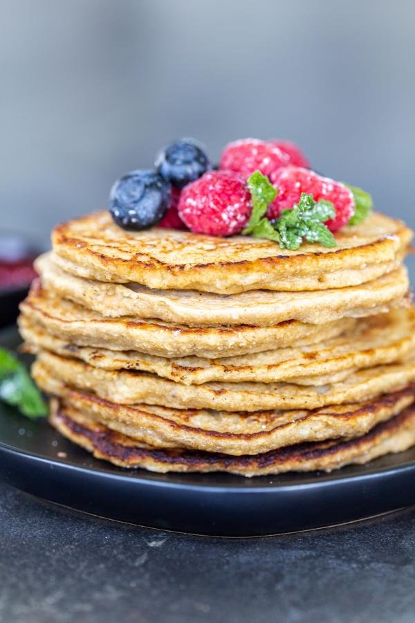 Tas de crêpes à la banane et avoine sur une assiette avec des fruits.