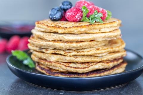 Tas de crêpes à la banane et avoine sur une assiette avec des fruits.