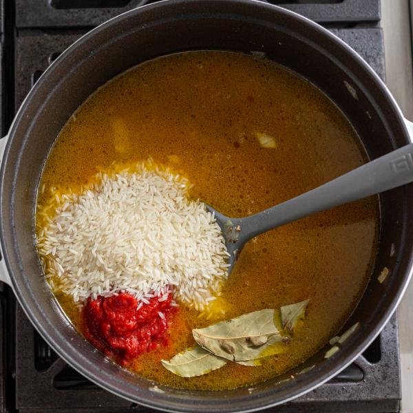 bouillon et riz dans une casserole avec de la pâte de tomate et des feuilles de laurier