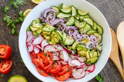 Salade dans un bol, tomates, radis, avocat, oignon et concombre, avec une sauce au-dessus